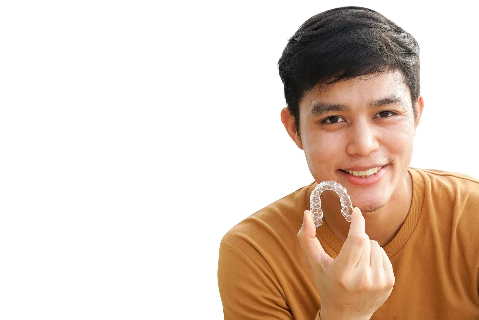 Teenager smiling while holding a clear aligner for orthodontic treatment
